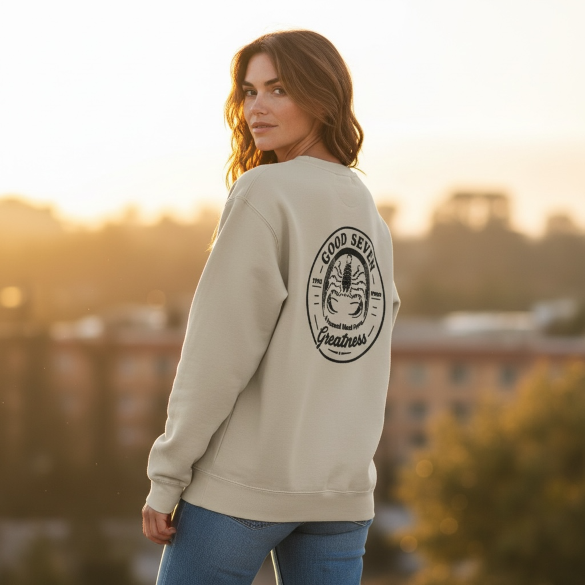 Woman wearing a beige sweatshirt with a logo and text, standing outdoors with a blurred background